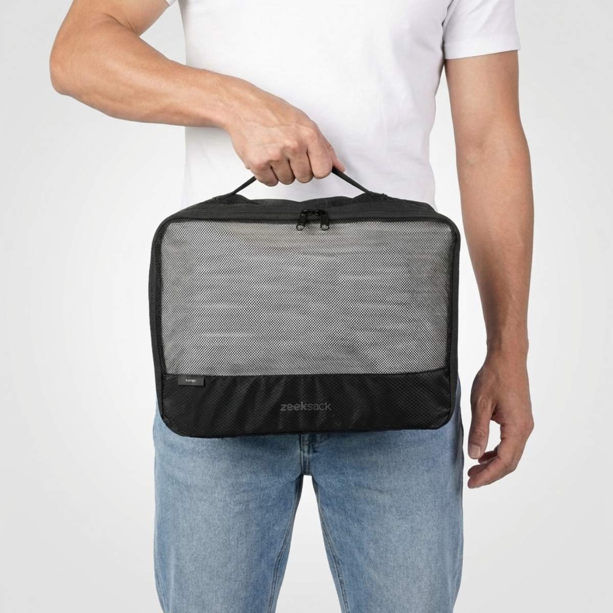 Mann in weißem T-Shirt und Jeans hält einen großen schwarzen Packwürfel mit Netzfach auf der Vorderseite.