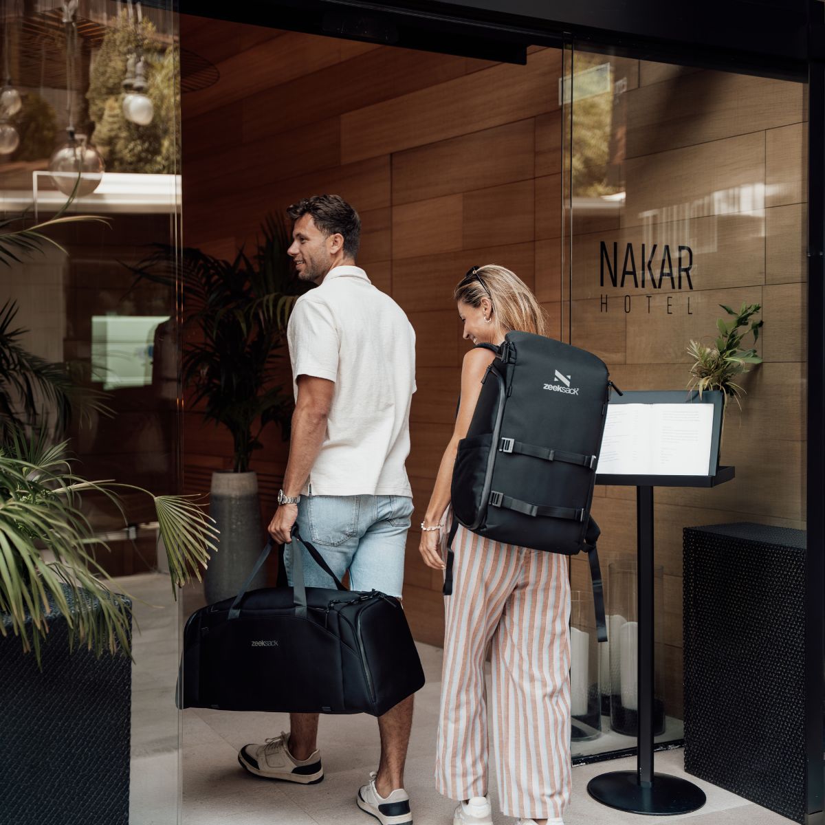 Zeeksack - Frau mit The Organizer 30L auf dem Rücken und Mann mit The Weekender 50L in der Hand auf dem Weg in ein Hotel.