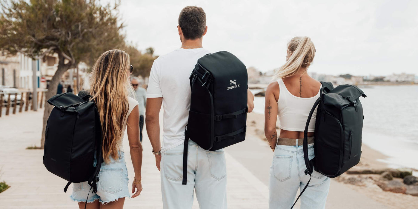 Drei Personen mit Zeeksack Rucksäcken spazieren am Strand entlang – stilvoll und bereit für jedes Abenteuer