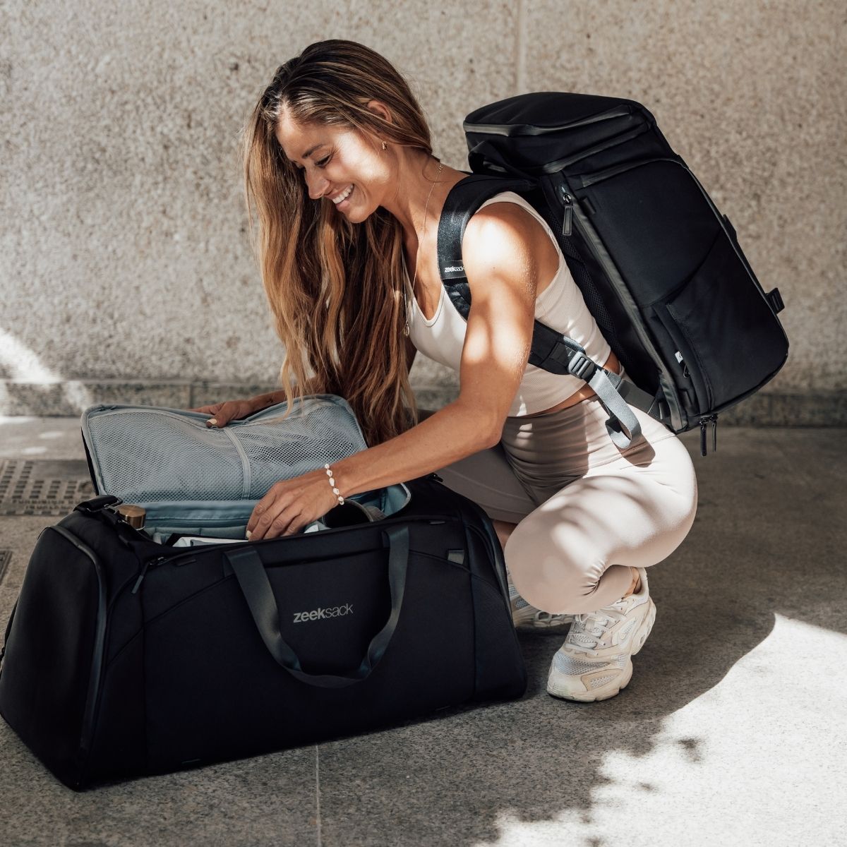 Frau mit dem Zeeksack Organizer auf dem Rücken packt eine Duffelbag – ideal für Reisen, Training und Alltag