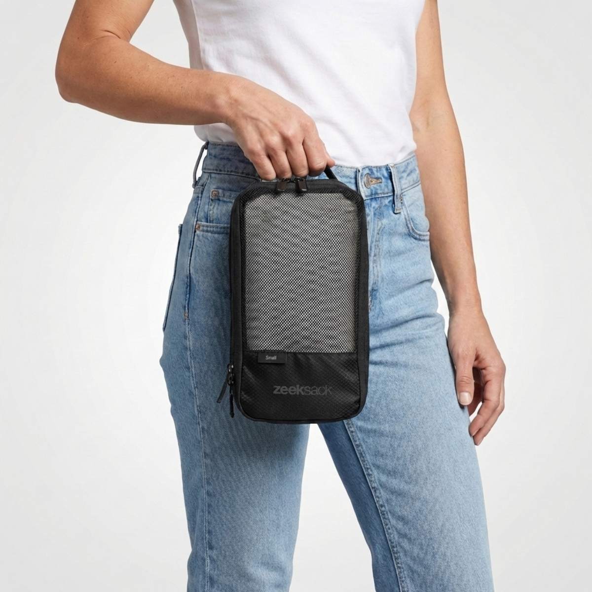 Frau in weißem T-Shirt und Jeans hält einen schwarzen Packwürfel mit Netzfach auf der Vorderseite.
