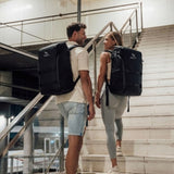 Zeeksack - Mann und Frau mit The Organizer 30L auf dem Rücken auf dem Weg eine Treppe hinauf.
