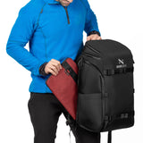 Mann steckt eine rote Laptophülle seitlich in das Laptopfach des Zeeksack Organizer Rucksacks