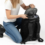 Frau kniet und legt Kopfhörer in das obere Fach eines schwarzen Zeeksack Rucksacks, praktischer Rucksack mit organisiertem Stauraum für Alltag und Reisen.