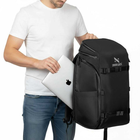Mann steckt einen Laptop in das vordere Fach eines schwarzen Zeeksack Rucksacks, moderner Rucksack mit Laptopfach für Arbeit und Reisen.