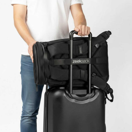 Schwarzer Zeeksack Rucksack befestigt am Griff eines Rollkoffers mit Trolley-Gurt, praktischer Rucksack für einfaches Reisen.