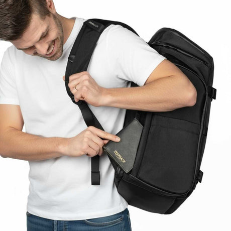 Mann verstaut eine schwarze Geldbörse in der versteckten Rückentasche eines Zeeksack Rucksacks, sicherer Rucksack mit Anti-Diebstahl-Fach.
